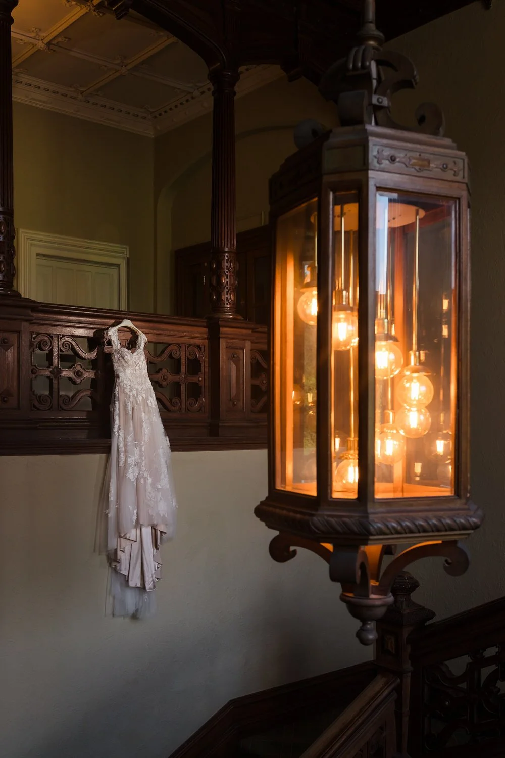 Wedding dress hanging on the carved staircase balustrade beside a period lantern at The Welcombe Hotel.