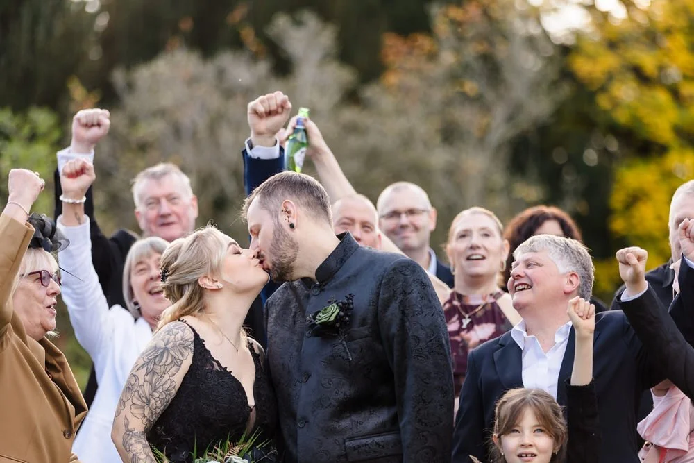 Wedding guests cheering and celebrating couple's kiss at Arley House Gardens, joyful group photography Worcestershire