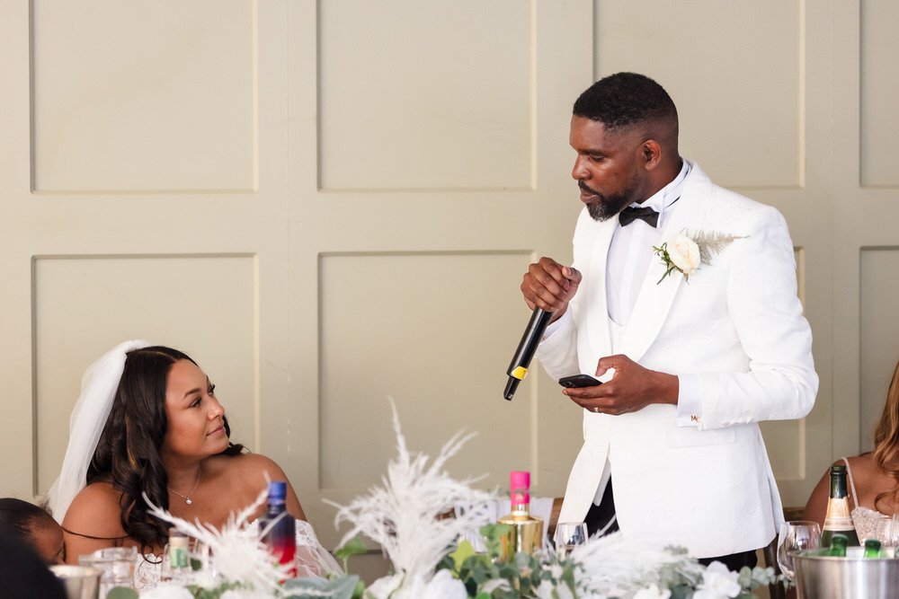 Groom giving his speech with phone in hand as the bride looks up at him during the wedding breakfast at Hogarths Hotel Solihull.