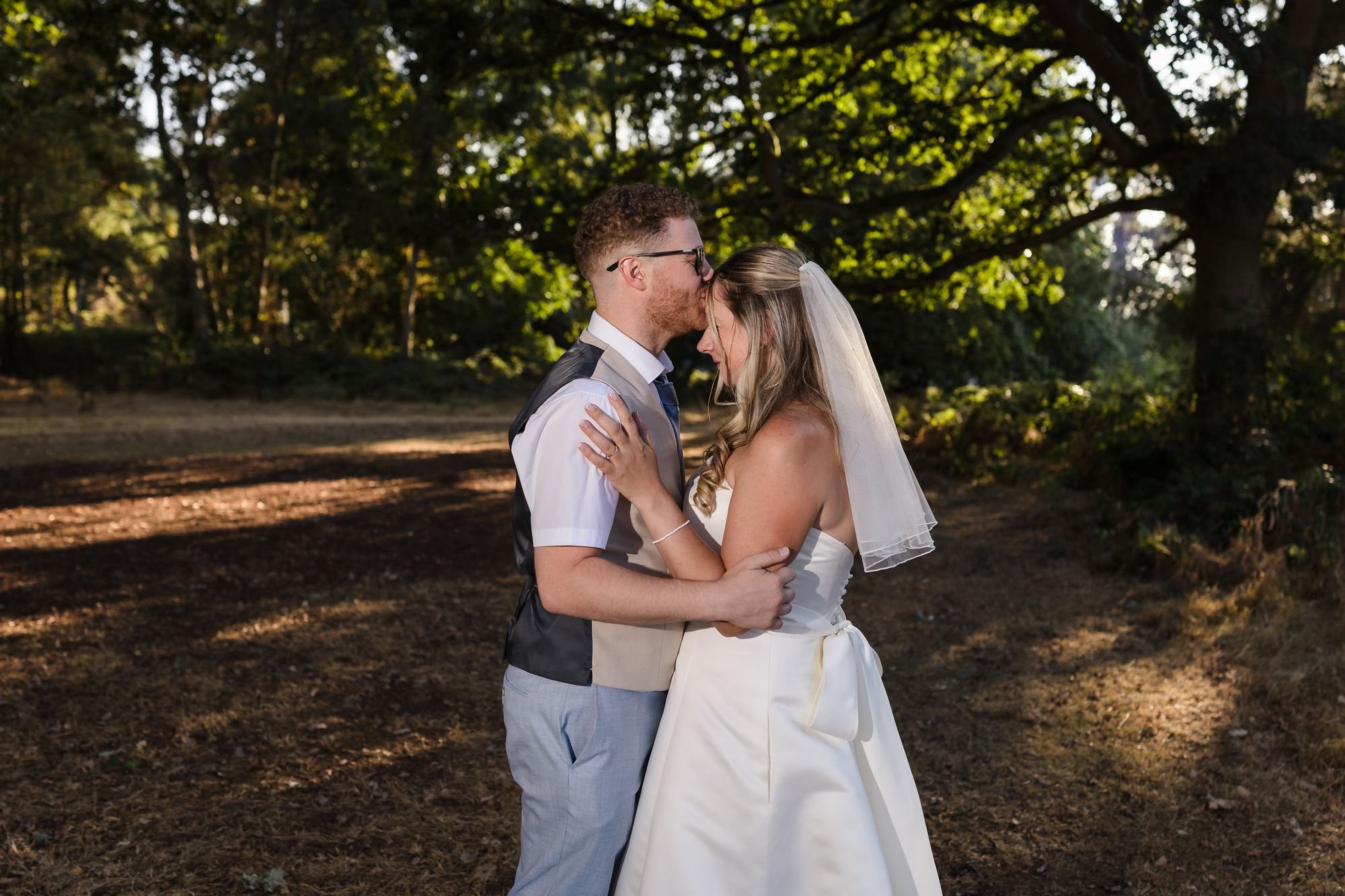 Josh kissing Cheryl's forehead in low evening light under the trees at Hogarths Stone Manor