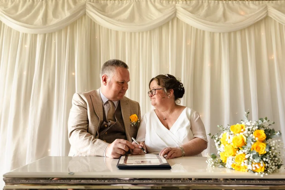 Bride and groom signing the register at their De Vere Cotswold Water Park wedding ceremony