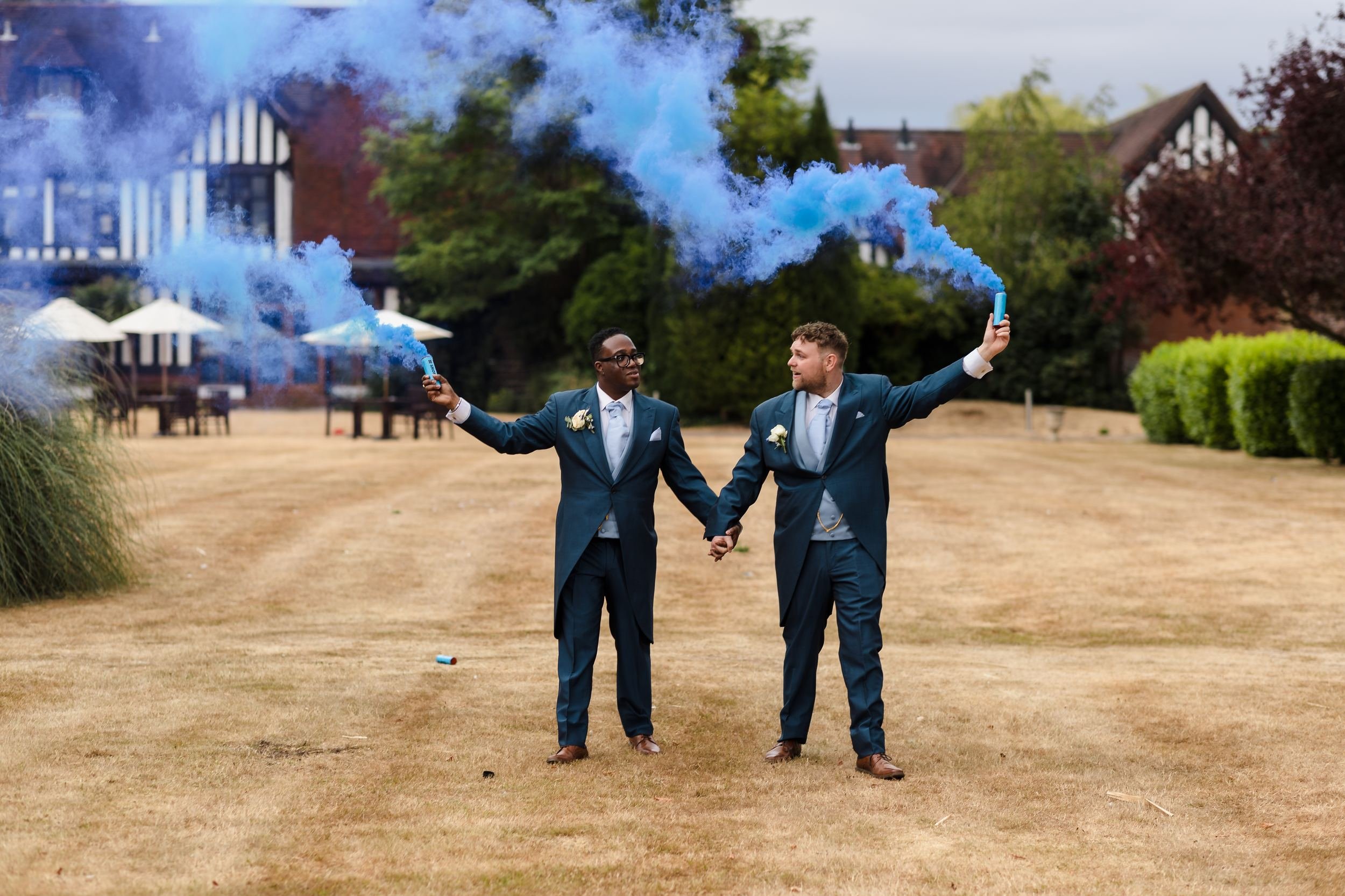 Liam and Shaun holding hands on the main lawn with arms outstretched, trailing plumes of blue smoke in front of Hogarths Stone Manor