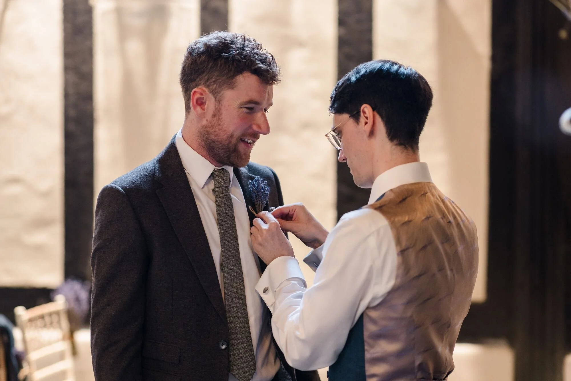 Groomsman fixing a buttonhole before the ceremony in the Great Hall at The Commandery, Worcester, by Once in a Lifetime Photography