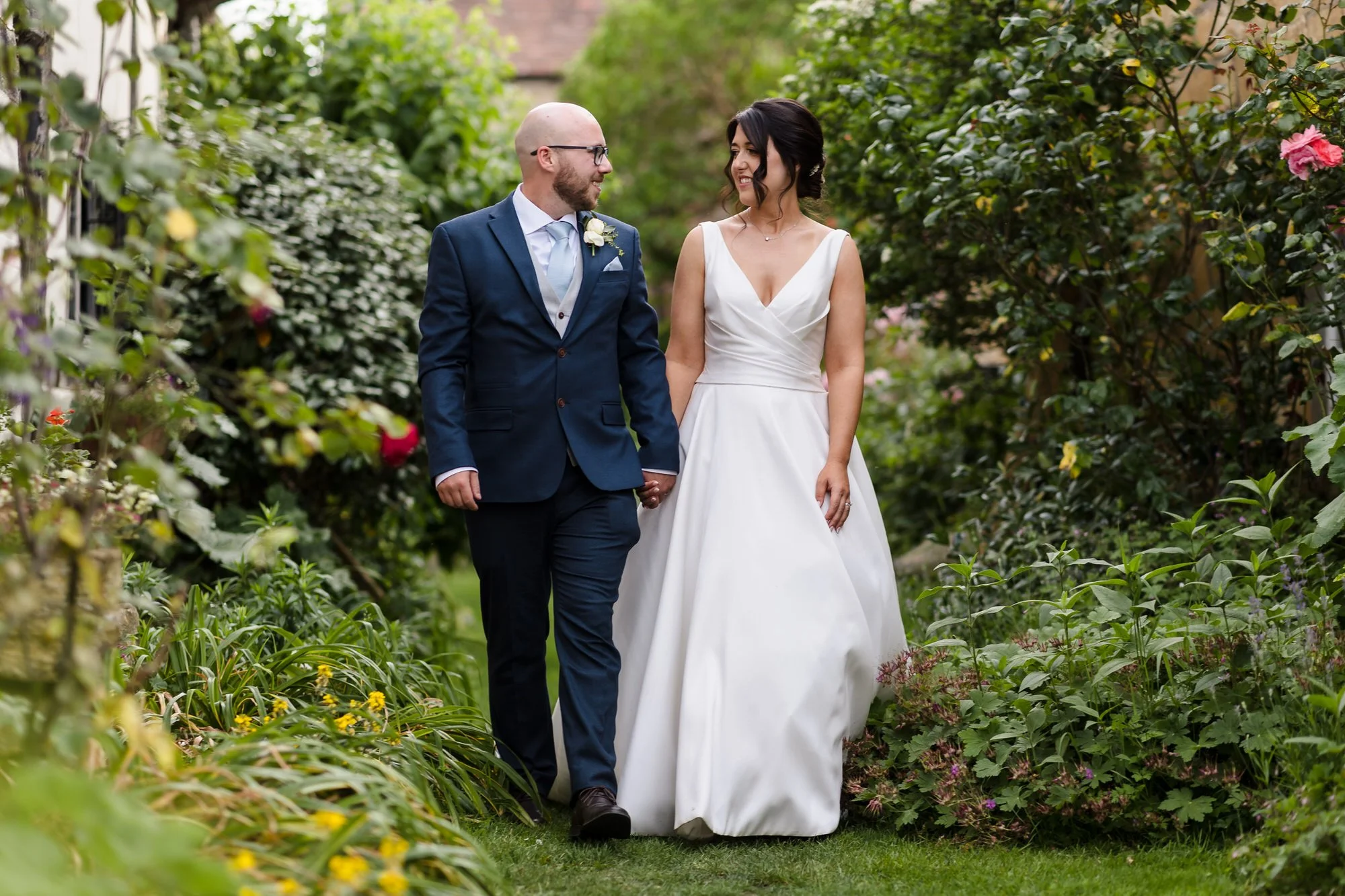 Bride and groom walking hand in hand through a flower-lined garden path at their Worcestershire wedding