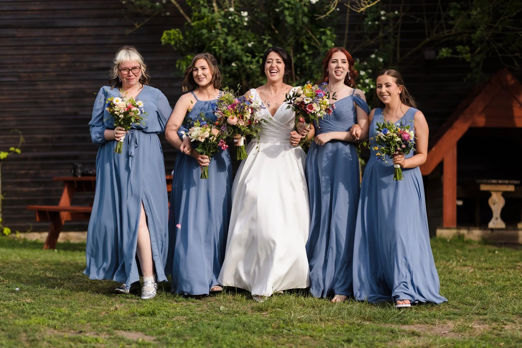 Bride walking with her bridesmaids in dusty blue dresses carrying wildflower bouquets at The Fleece Inn, Worcestershire