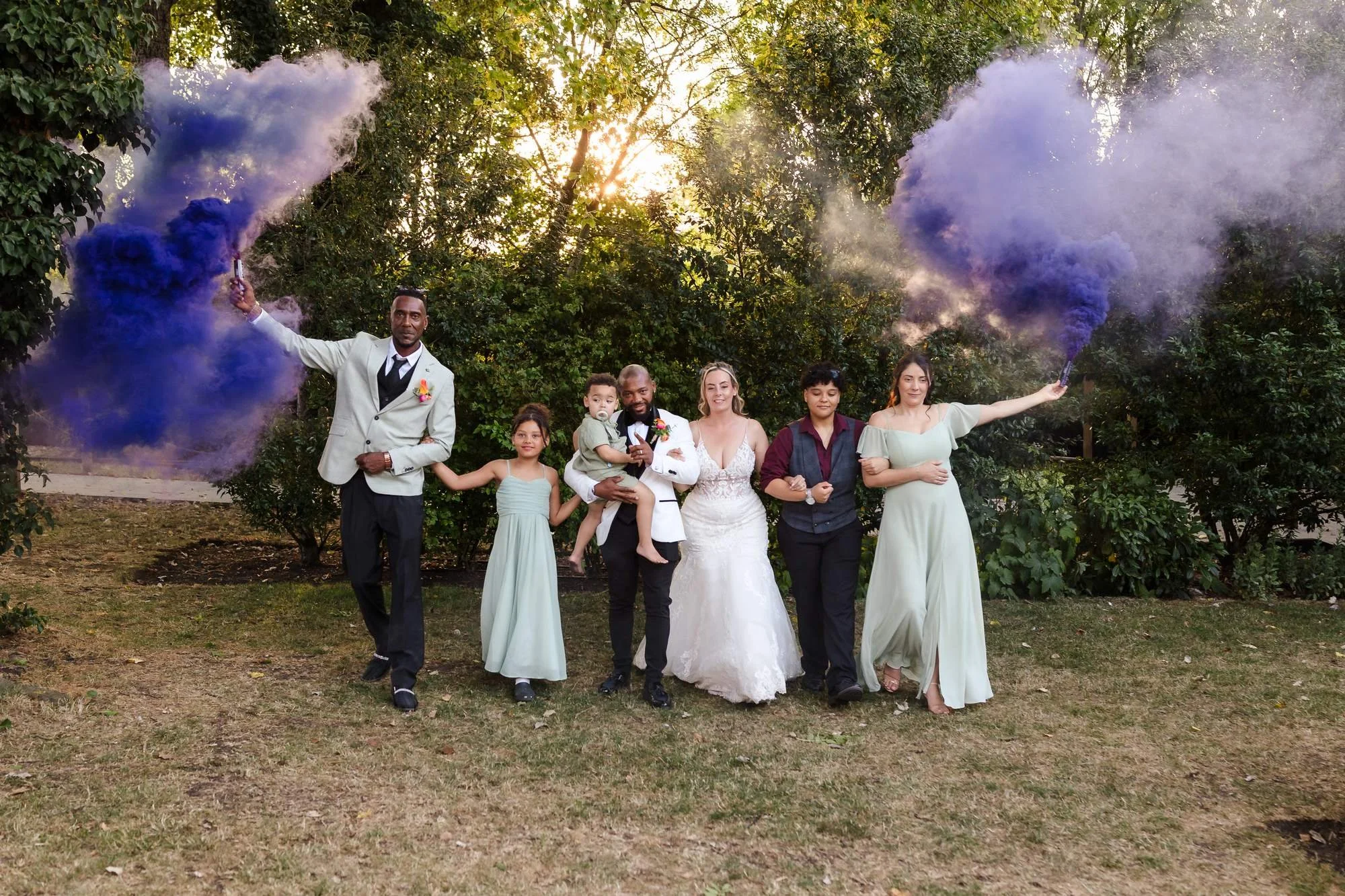 Bridal party walking towards the camera with blue and purple smoke bombs in the gardens at Warwick House