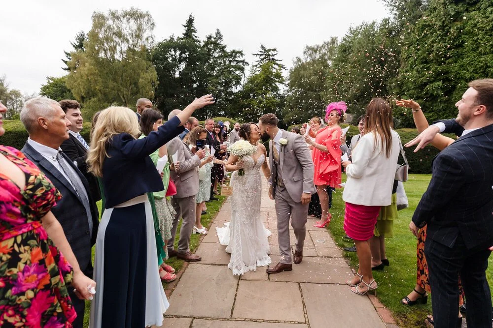 Bride and groom sharing a kiss whilst confetti is thrown