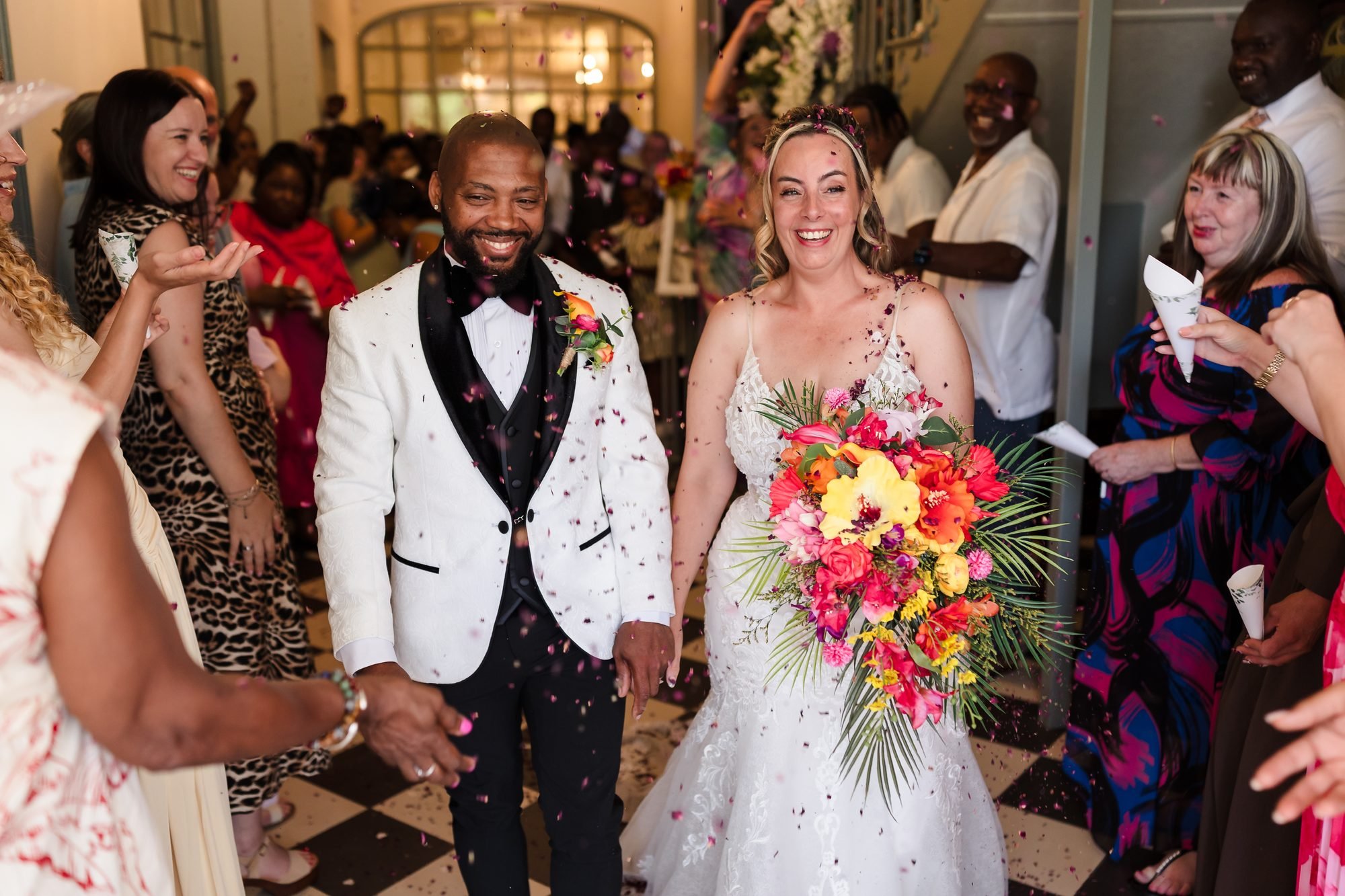 Bride and groom laughing through a shower of confetti in the hallway at Warwick House