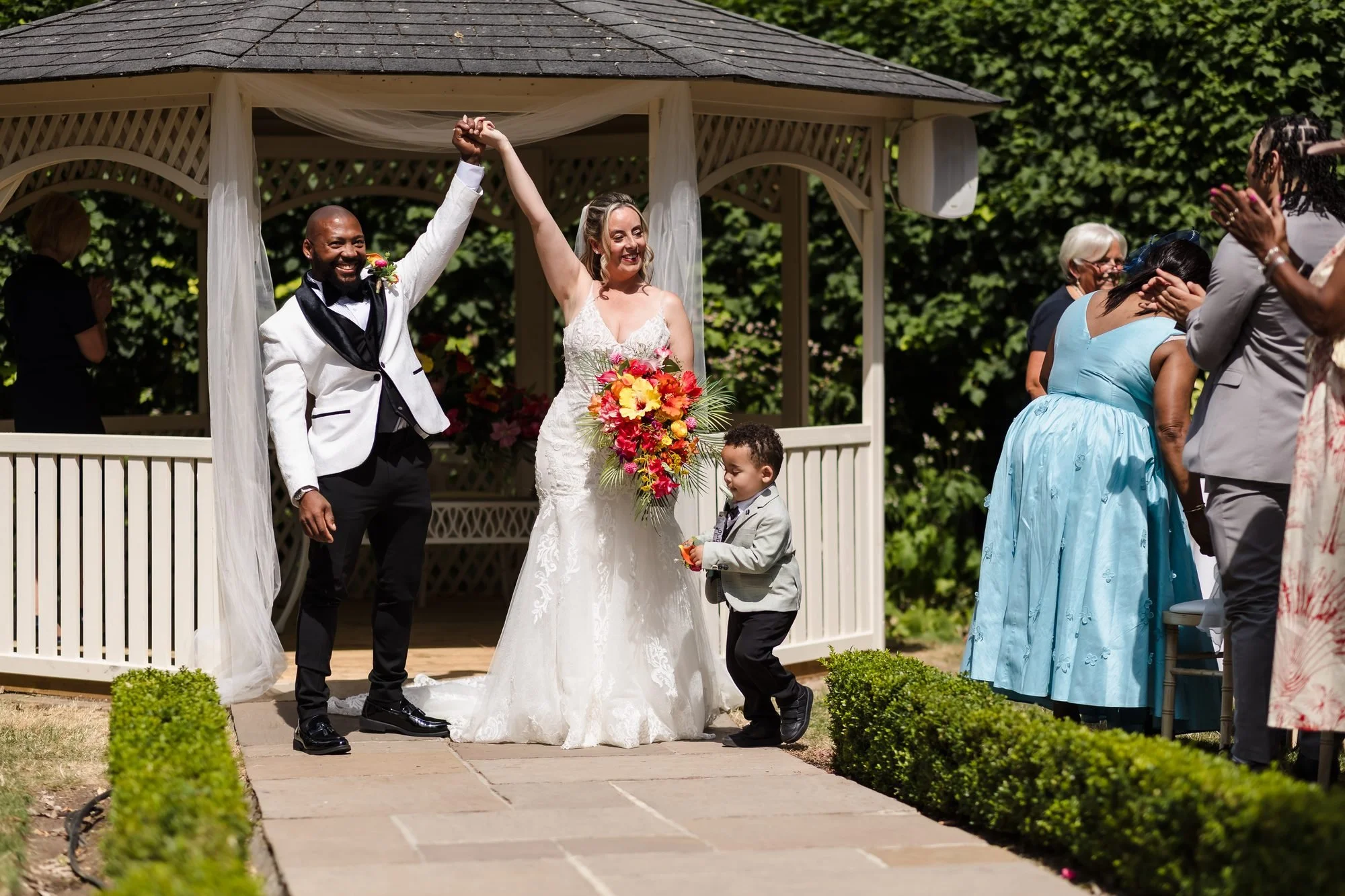 Newlyweds raising their arms in celebration in front of the gazebo as guests cheer at Warwick House