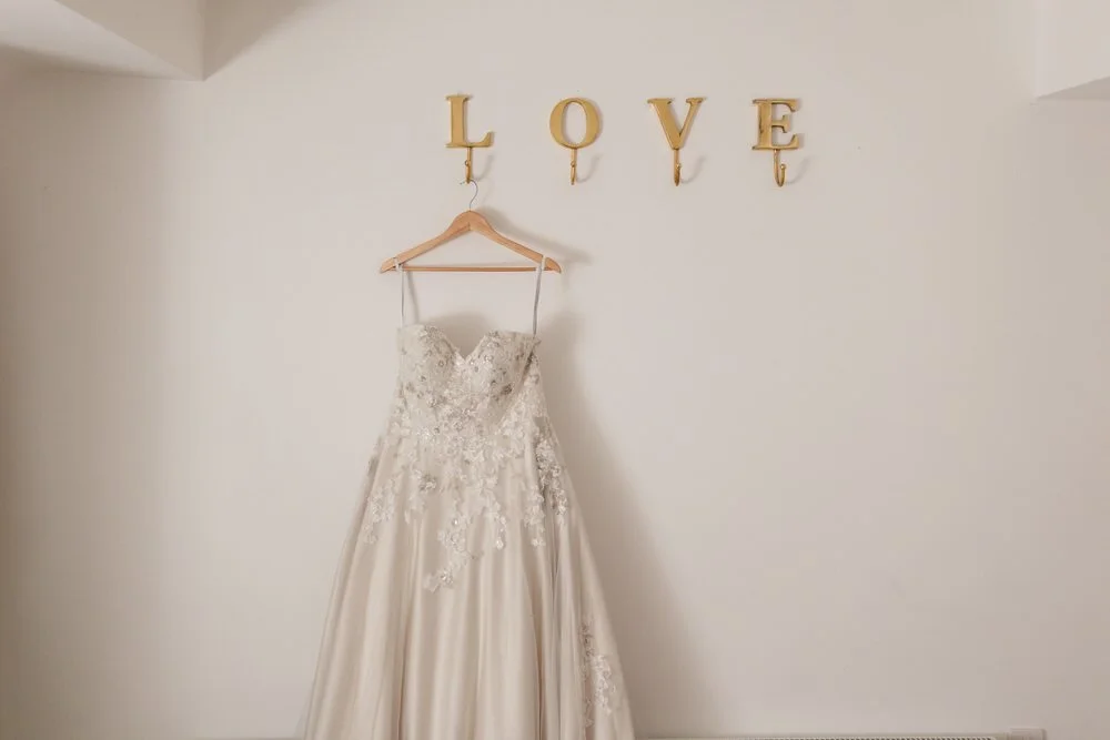 Bride's wedding dress hanging beneath a gold LOVE sign before getting ready at Huntsmill Farm.