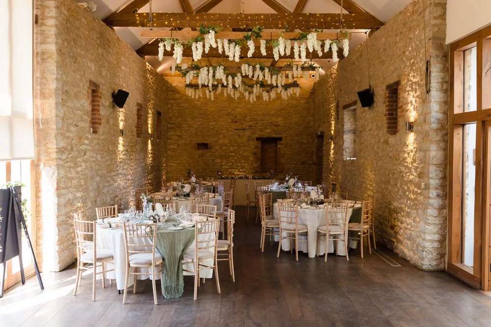 Barn reception room at Huntsmill Farm dressed with sage green linen and a hanging white floral installation.