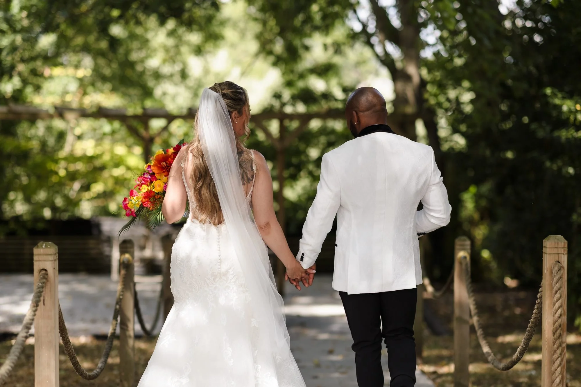 Bride and groom walking hand in hand along a rope-edged garden path at Warwick House, seen from behind