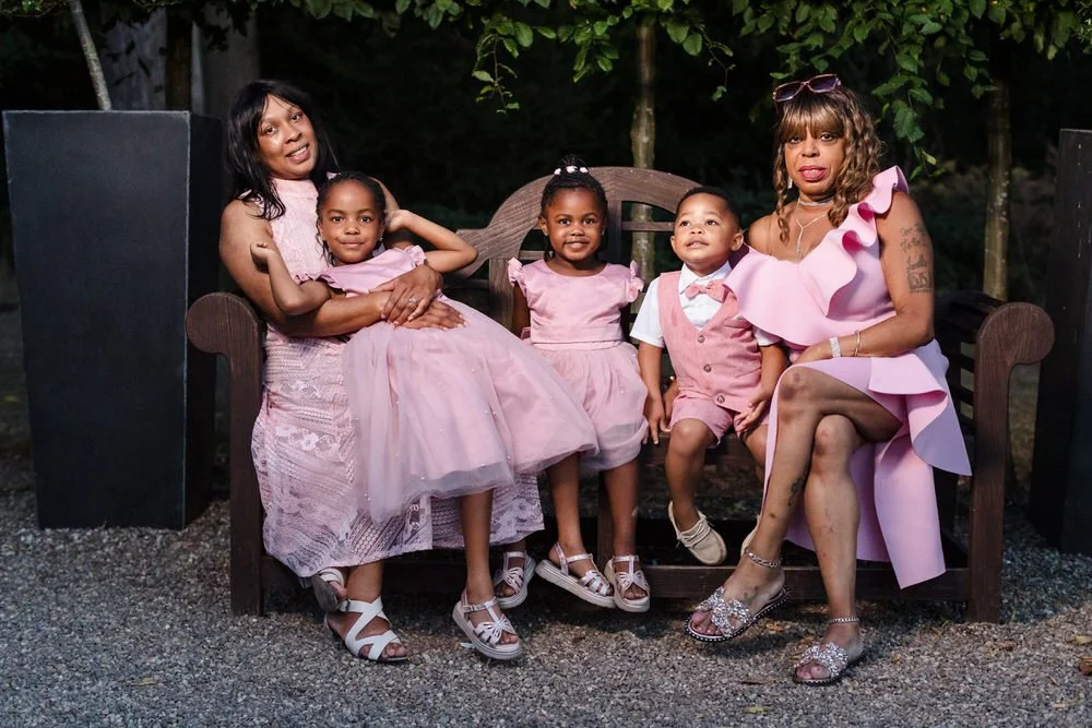 Family group portrait on the bench in the grounds of Hogarths Hotel Solihull, two women and three young children all dressed in pink — wedding photography by Once in a Lifetime Photography, Worcestershire