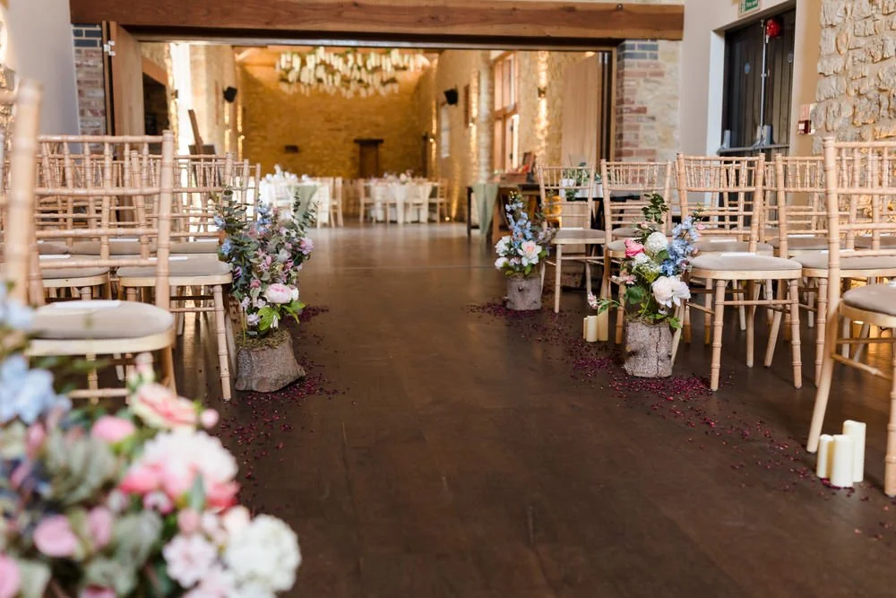 Ceremony aisle inside the barn at Huntsmill Farm, dressed with floral arrangements and scattered petals.
