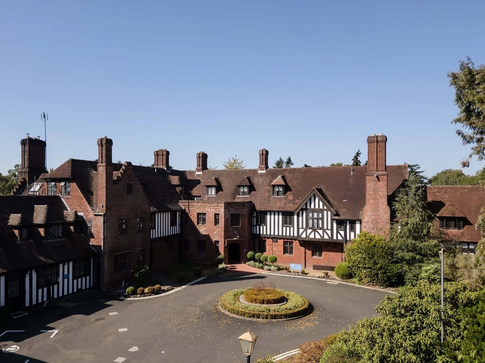 Aerial view of the Tudor-style brick and timber front of Hogarths Stone Manor and its turning circle on a clear summer morning