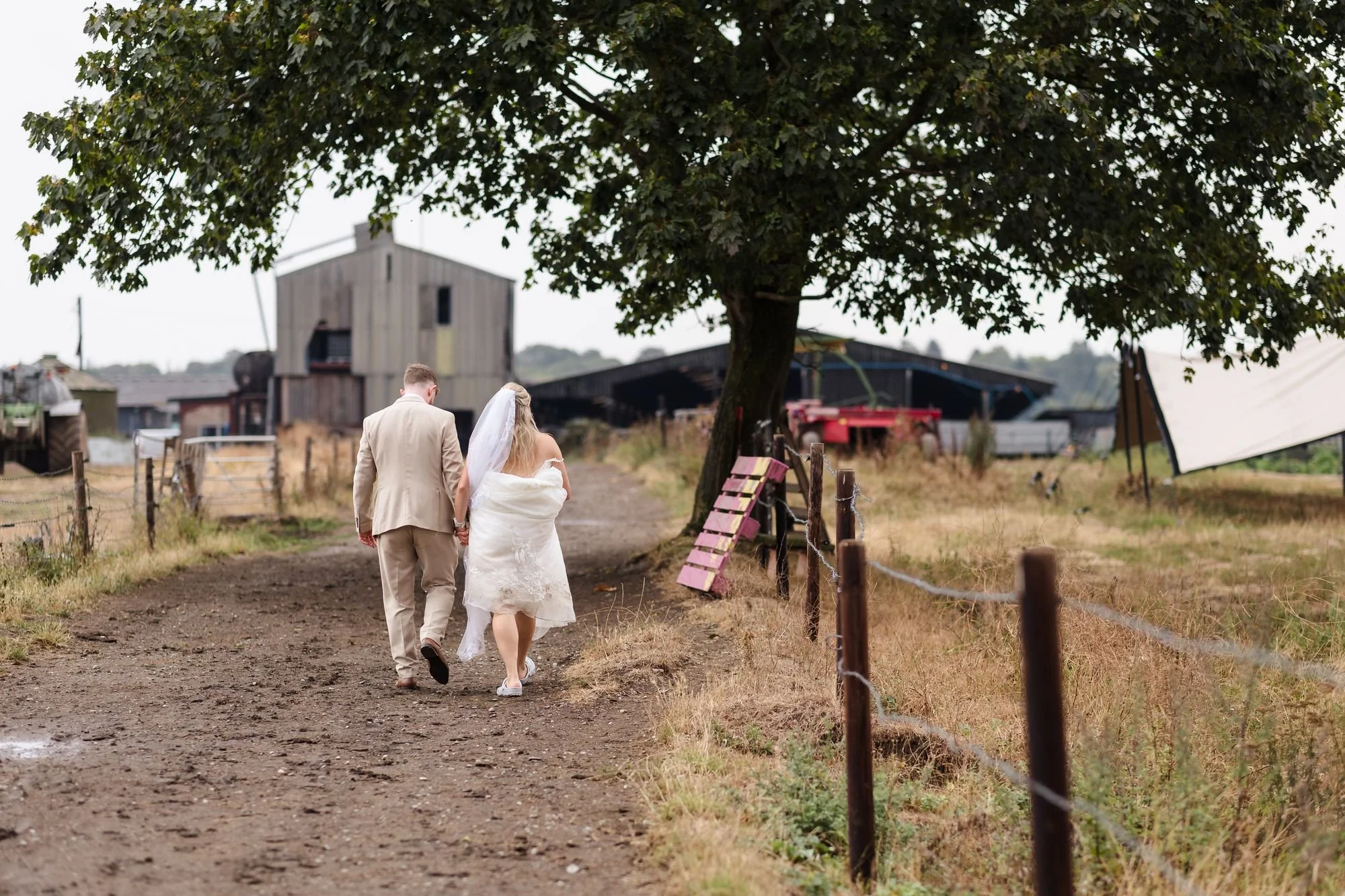 Abbie and Sean walking hand in hand down the farm track towards the barns at Bennetts Willow Barn