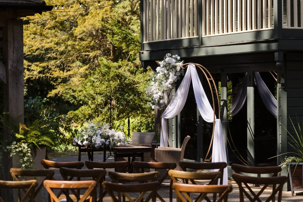 Gold hoop arch with white draping and wicker chairs set for the outdoor island ceremony at Hogarths Hotel Solihull.