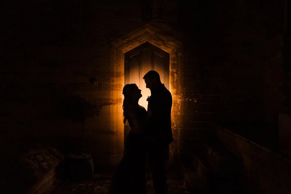 Silhouette of a couple standing close together in front of an illuminated arched doorway at night at Arley House and Gardens.