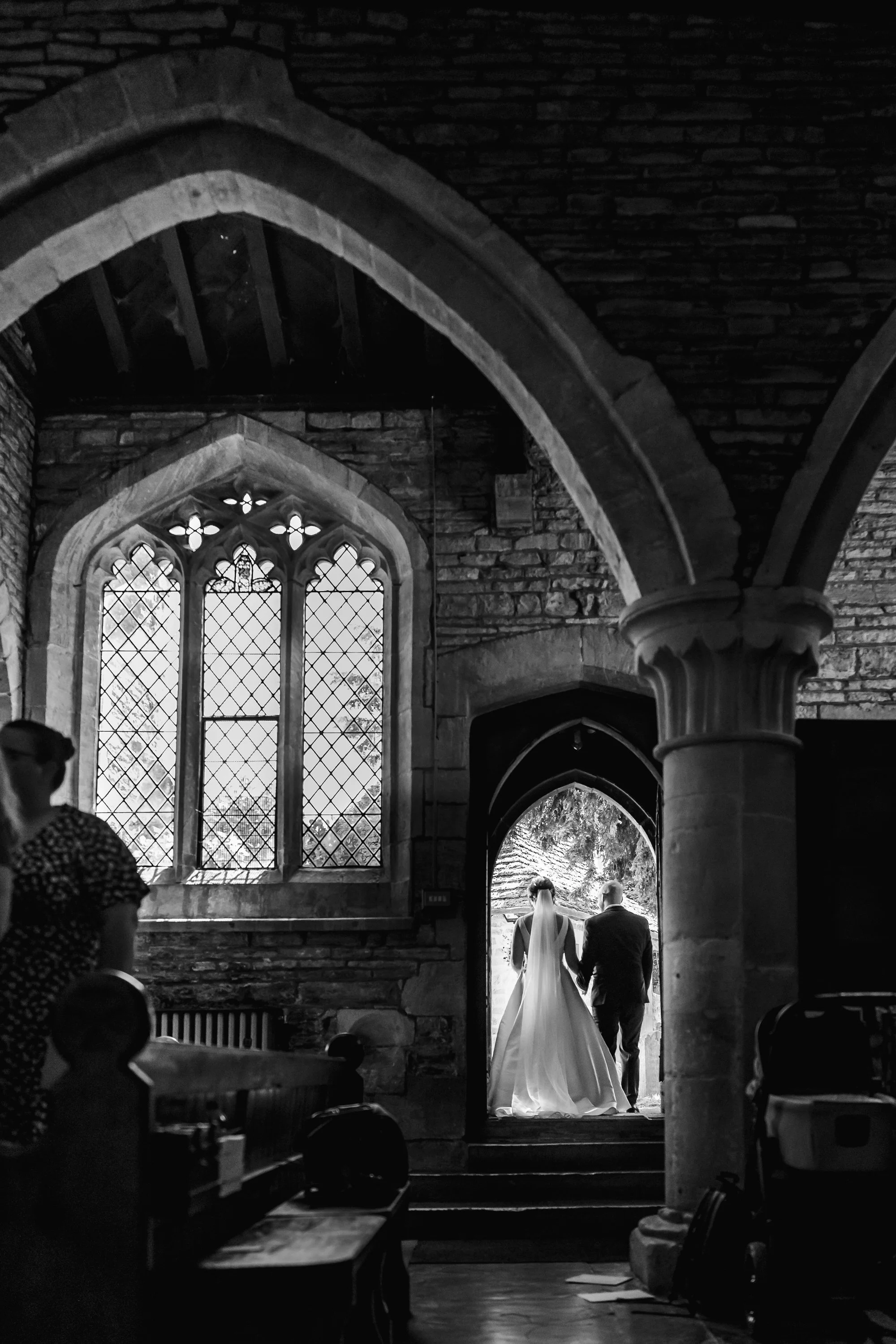 Bride and her father silhouetted in a stone doorway at St Leonard's Church, black and white documentary wedding photography