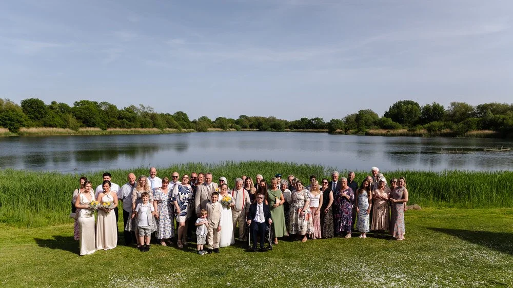 Full wedding party group photo beside the lake at De Vere Cotswold Water Park