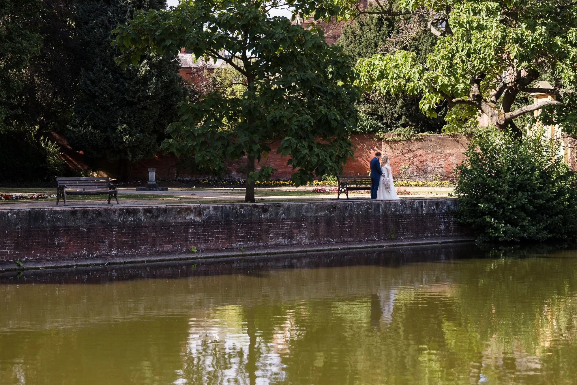 The couple photographed across the water at Minster Pool, Lichfield, wedding photography by Once in a Lifetime Photography.