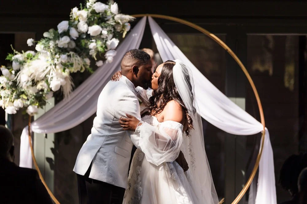 Bride and groom sharing their first kiss within the gold hoop arch at Hogarths Hotel Solihull's island ceremony.