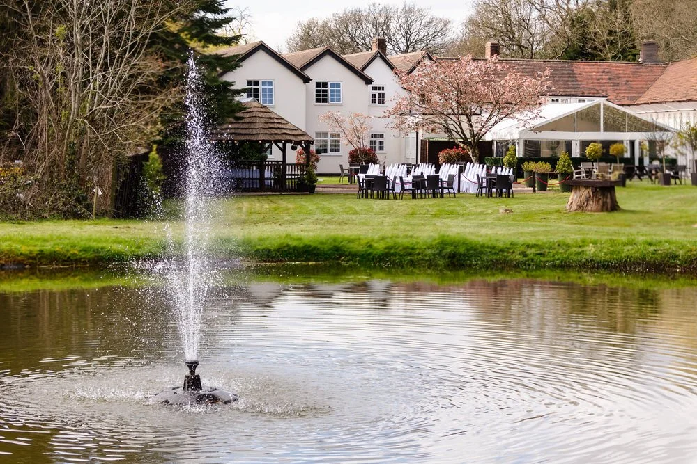 The Limes Country Lodge lake and fountain with outdoor wedding reception tables set up on the lawn — wedding photography by Paul Hickey