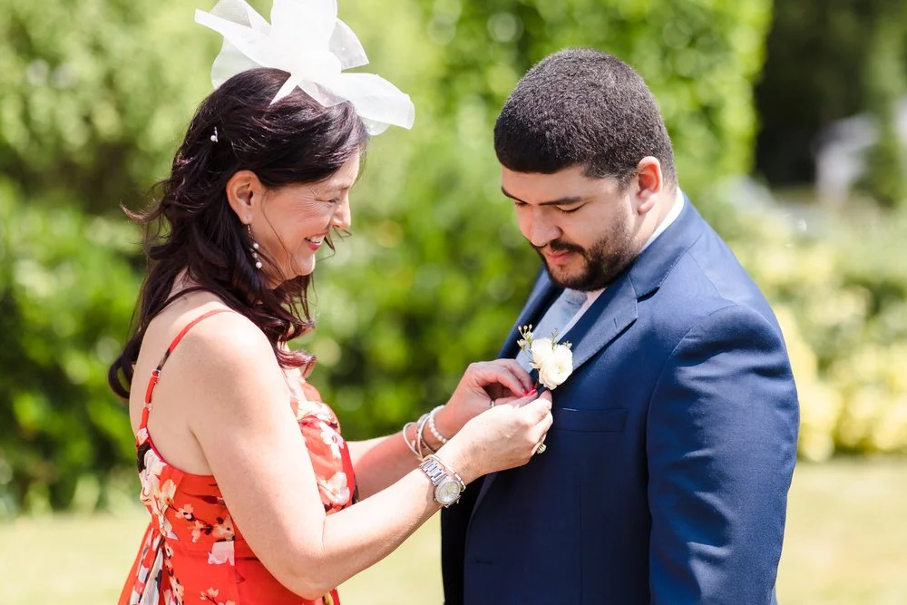 Groom has his boutonnière pinned by a relative in the sunshine outside in the gardens at Karma Salford Hall.