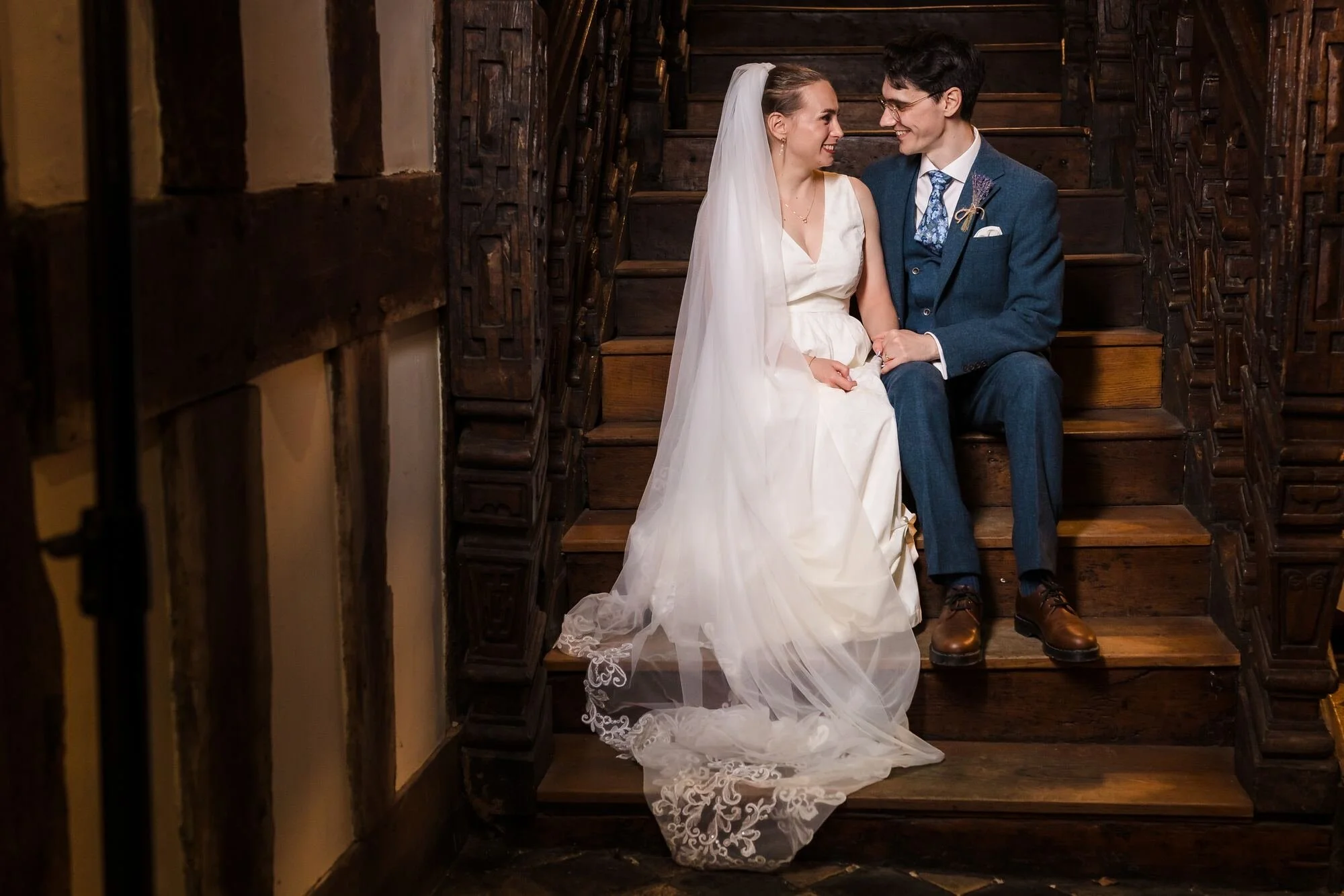 Isabelle and Chris sitting on the carved wooden staircase lit by a softbox at The Commandery, Worcester, by Once in a Lifetime Photography