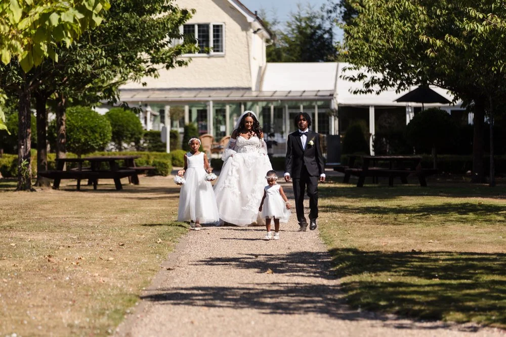 Bride, groom and flower girls walking through the gardens at Hogarths Hotel wedding venue.