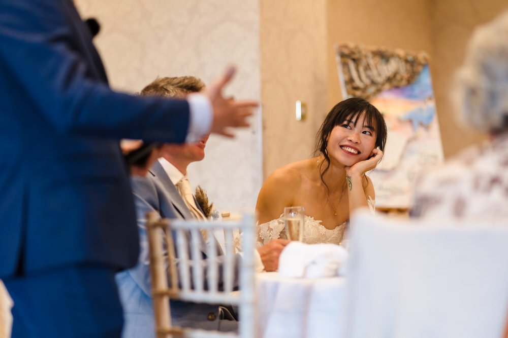 Bride Christine smiling while listening to speeches at The Welcombe Hotel wedding reception, Warwickshire.