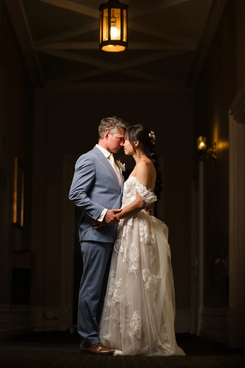 Christine and Greg lit by lantern light in a period corridor at The Welcombe Hotel during evening portraits.