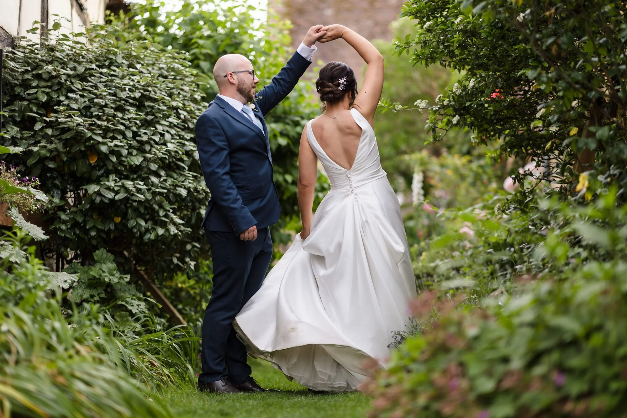 Groom twirling his bride among garden foliage, candid movement captured during couple portraits at a Worcestershire wedding