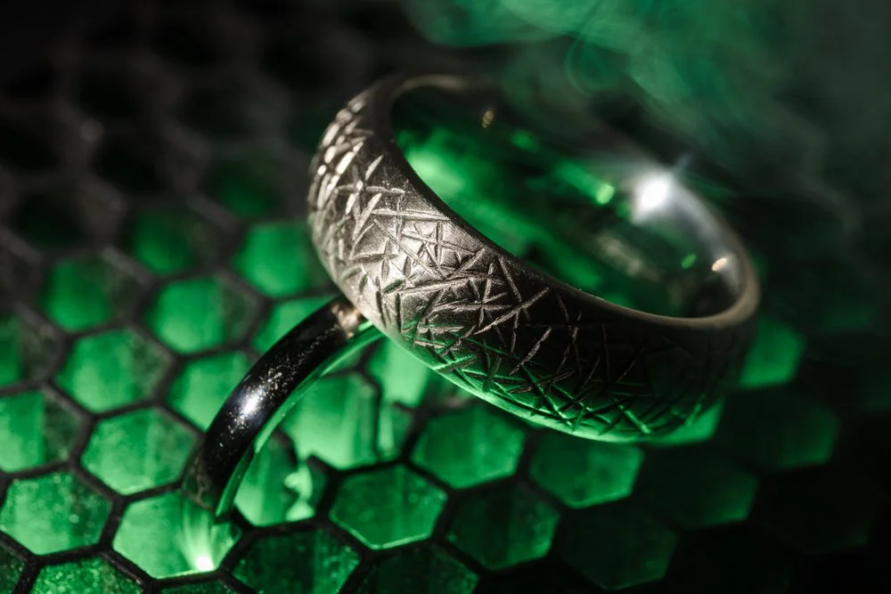 xMacro detail of patterned silver wedding bands on green gem surface, creative wedding ring photography Worcestershire