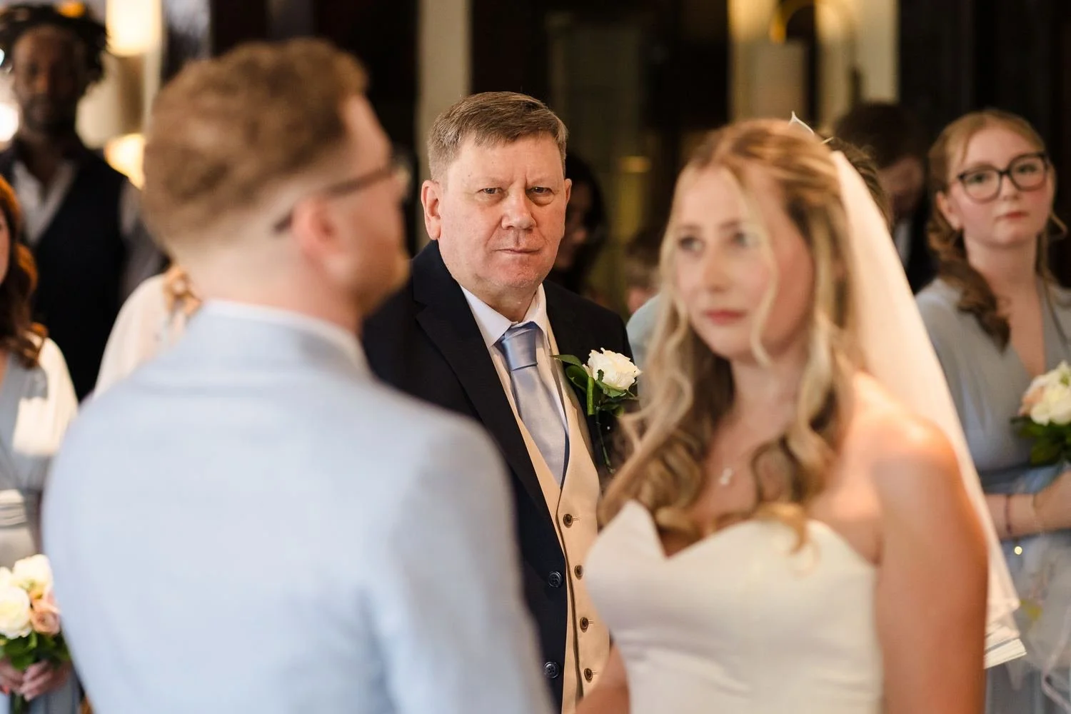 A guest in a navy suit watching closely as Cheryl and Josh say their vows