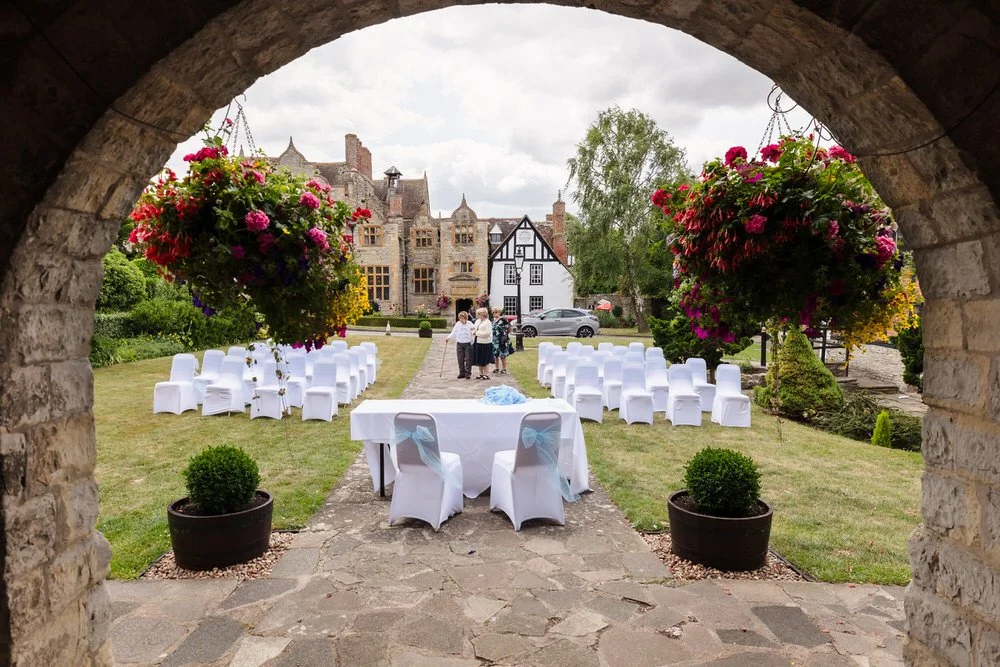 View through the archway onto the courtyard ceremony space at Karma Salford Hall, framed by hanging baskets.