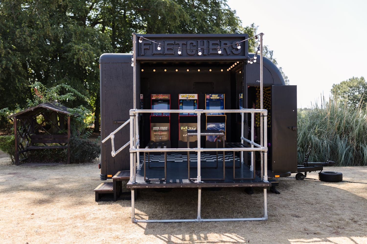 Mobile retro arcade trailer with Pac-Man machines set up on the lawn for wedding guests