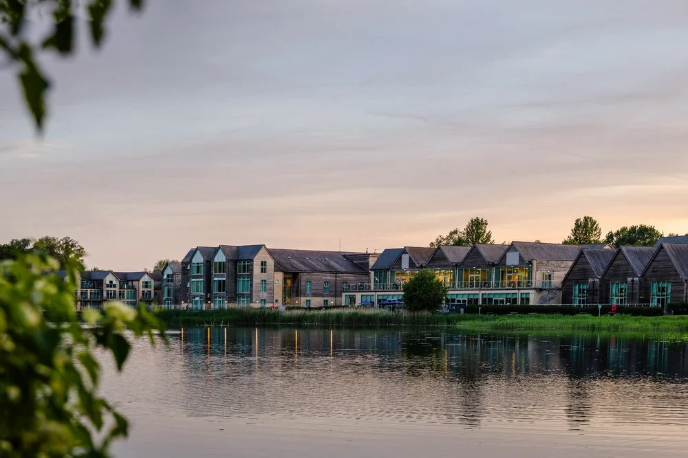 De Vere Cotswold Water Park hotel reflected in the lake at dusk, South Cerney