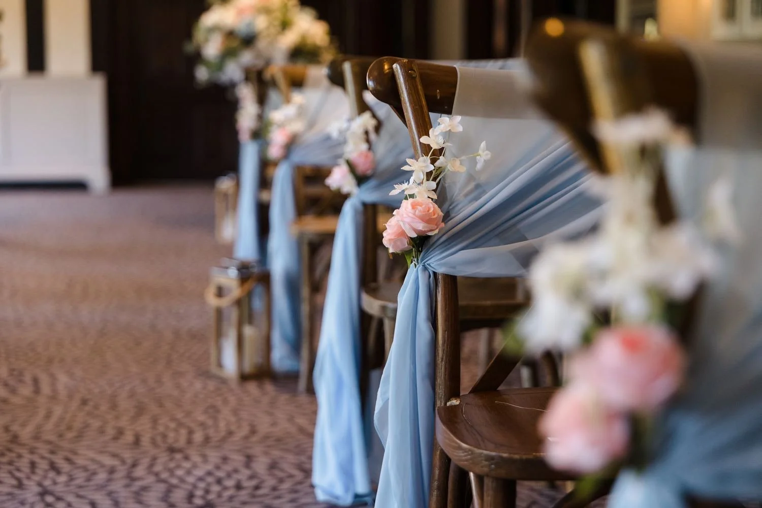 A row of ceremony chairs in the Drawing Room dressed with sky-blue drapes, pink roses and lanterns