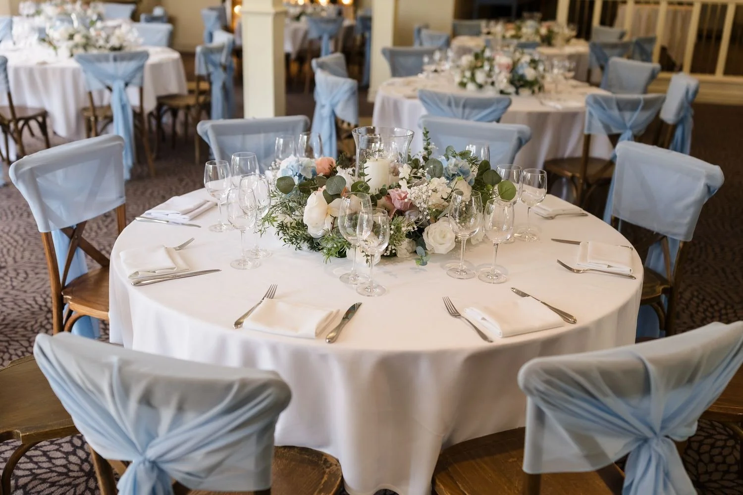 Garden Room table set for the wedding breakfast with sky-blue chair covers and a floral centrepiece
