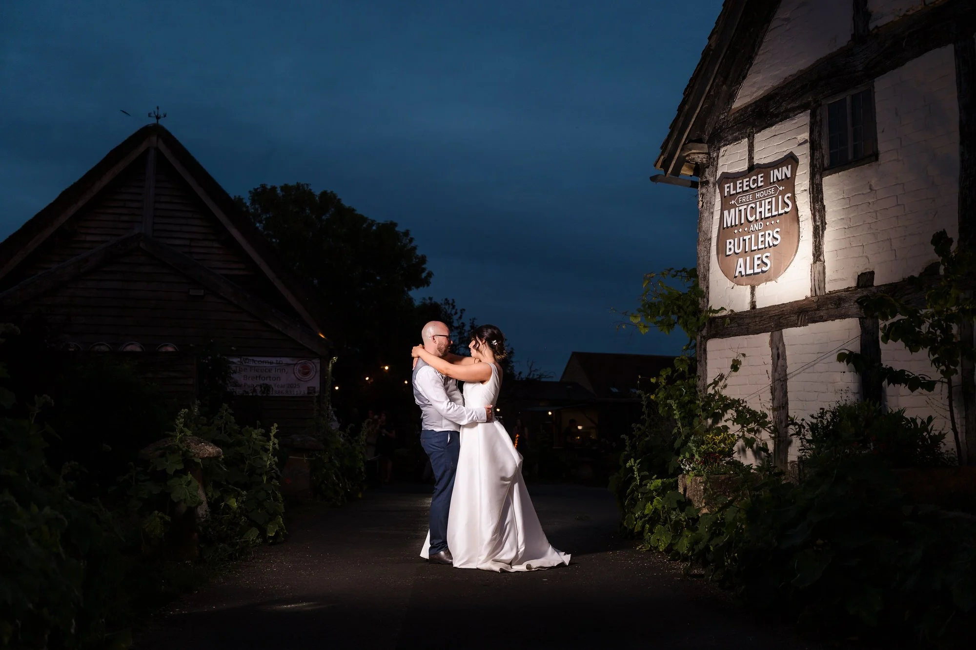 Bride and groom dancing at dusk outside The Fleece Inn, its illuminated pub sign lighting the Worcestershire courtyard