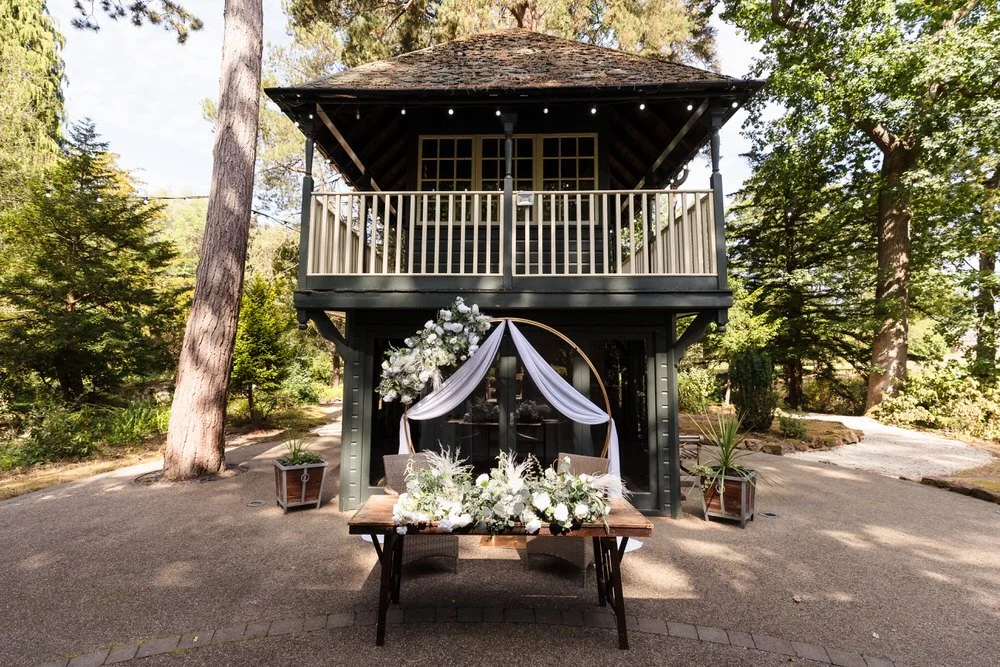 Outdoor wedding ceremony setup with floral arch and table in the woodland pavilion at Hogarths Hotel wedding venue.
