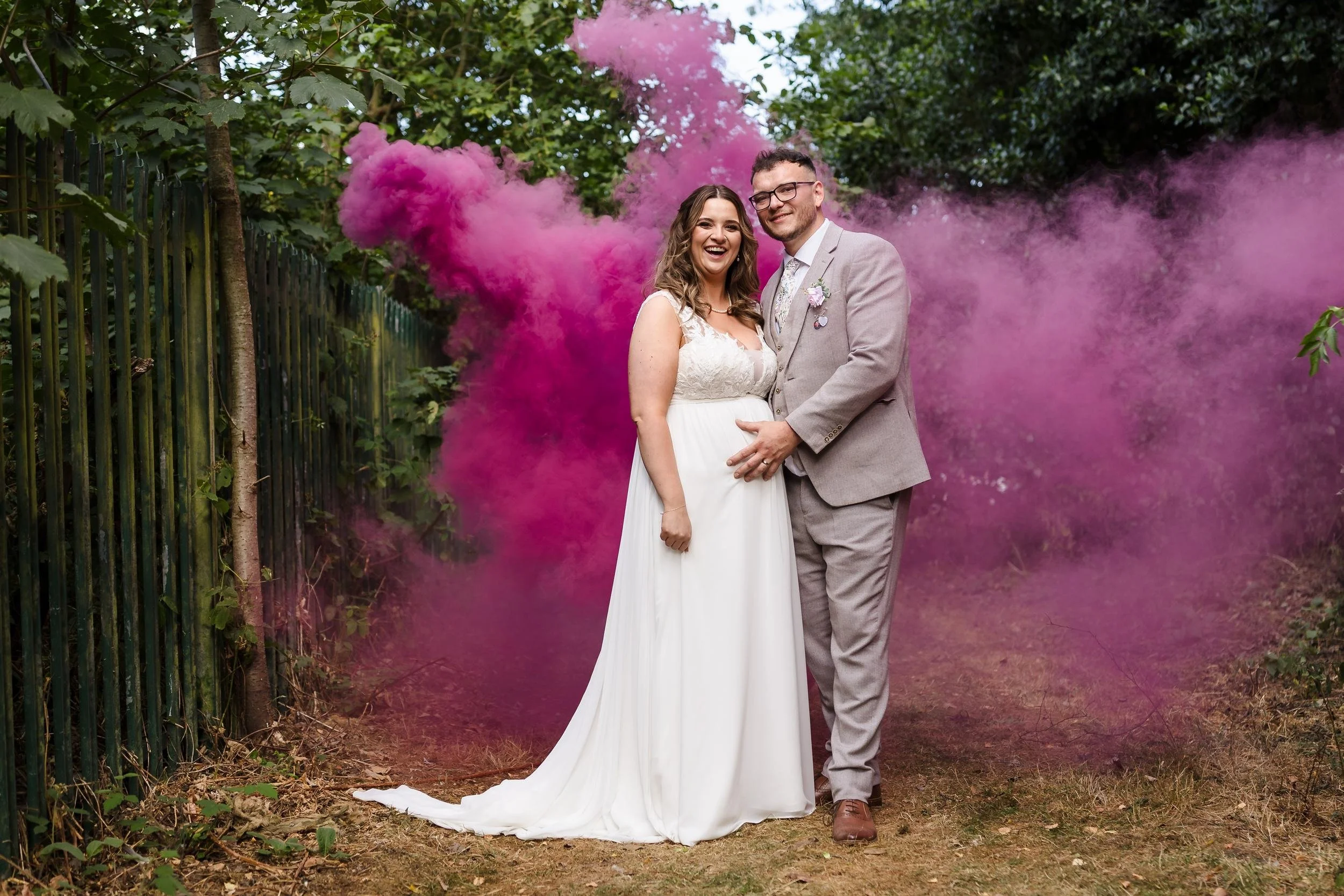 Holly and Dan smiling together in a cloud of pink smoke in the grounds of Nailcote Hall