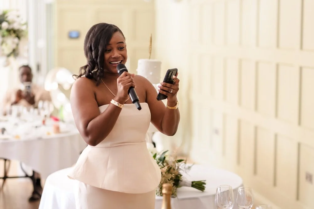 Bridesmaid in a blush dress giving a speech, reading notes from her phone, at the wedding reception at Hogarths Hotel Solihull
