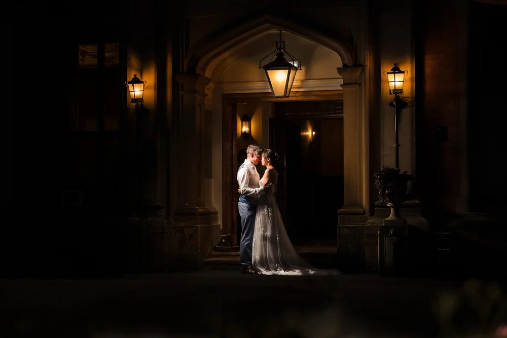 Christine and Greg under the lantern-lit entrance archway of The Welcombe Hotel at night.