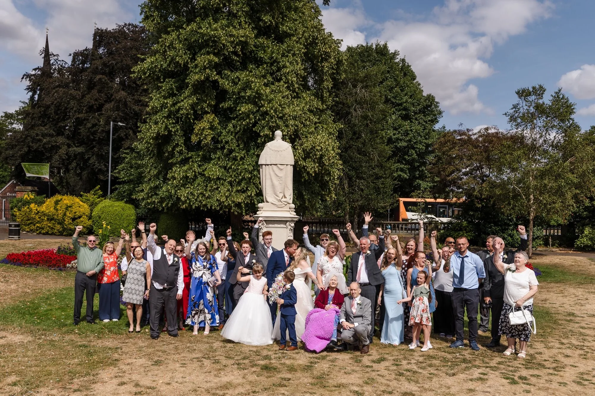 The full wedding group beside a monument in Museum Gardens, Lichfield, wedding photography by Once in a Lifetime Photography.