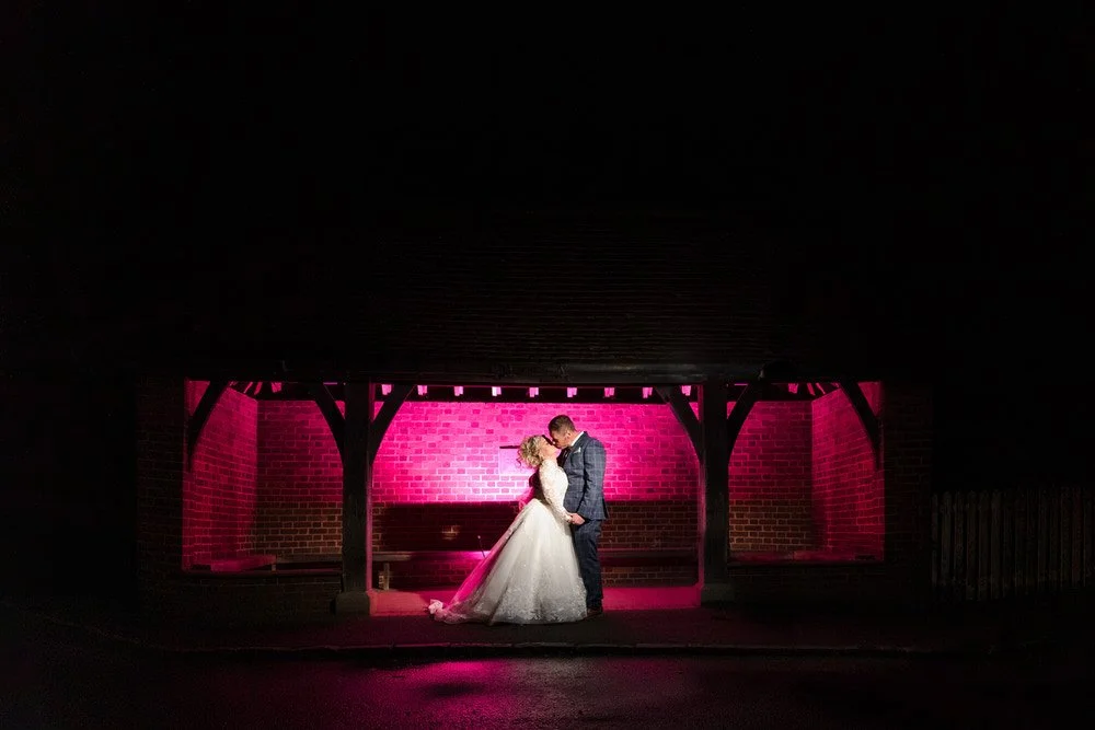 bride and groom kissing in a bus shelter at night