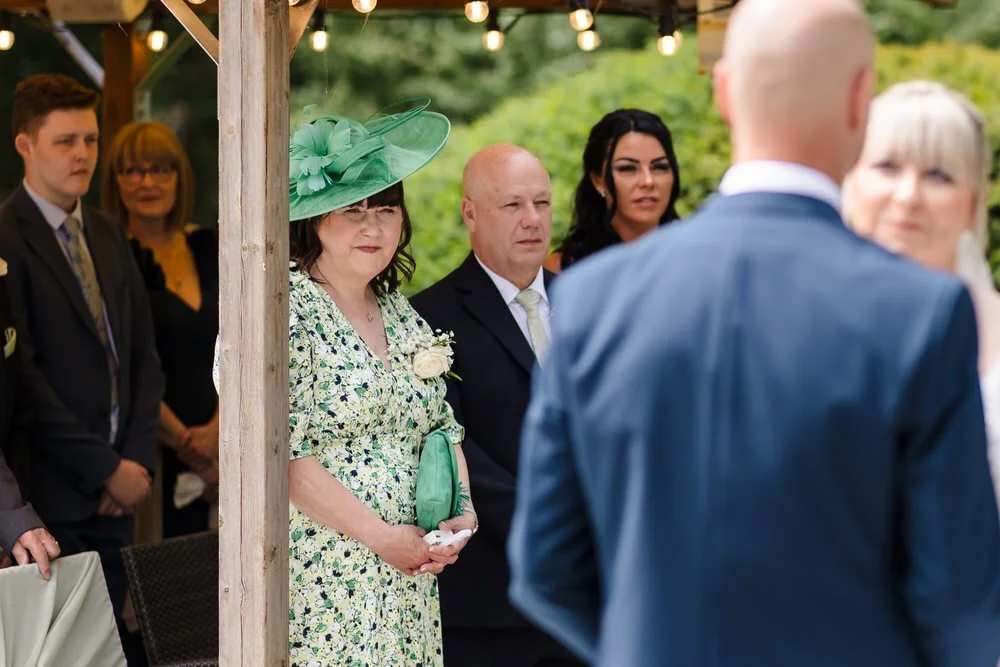 Wedding guest in a green fascinator and floral dress watching the outdoor ceremony at Hogarths Stone Manor
