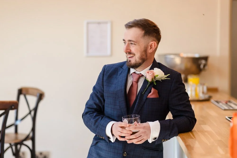 Groom smiling with whisky glass during wedding preparations at Bredenbury Court Barns