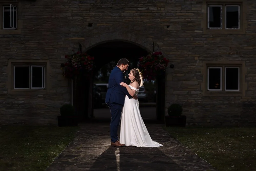 Creative wide shot at Karma Salford Hall with the couple centred beneath the Tudor gable and archway at dusk.
